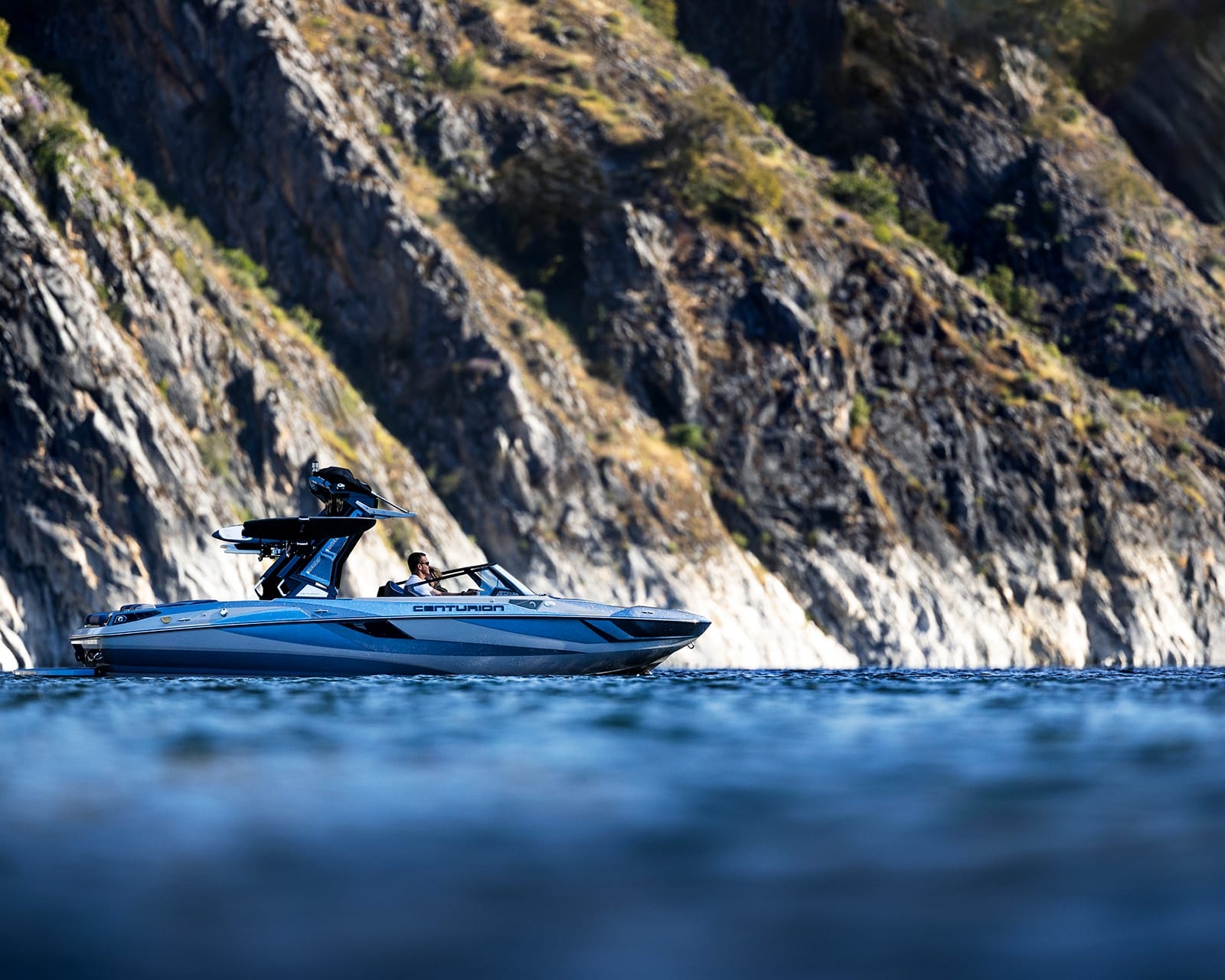 A Centurion Fi23 with a canopy floats on calm blue water near a rocky, tree-lined cliff.