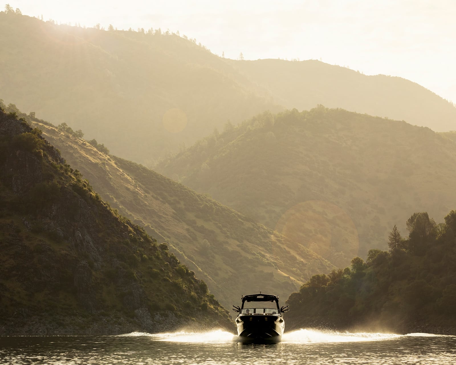 A Centurion Fi25 glides across a calm lake, sunlight shimmering on the water and mountains rising in the background.