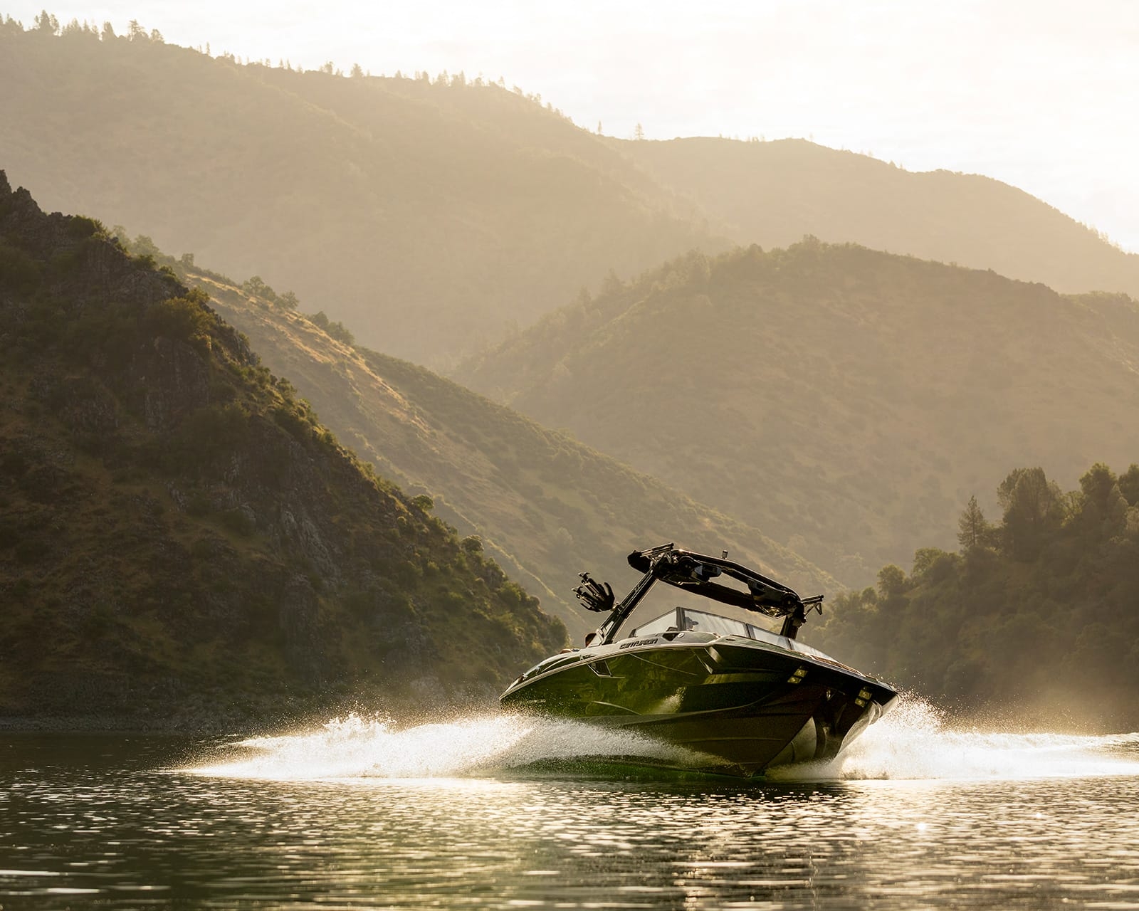 A Centurion Fi25 speeds across a calm lake, creating a wake, with tree-covered hills and a hazy sky in the background.