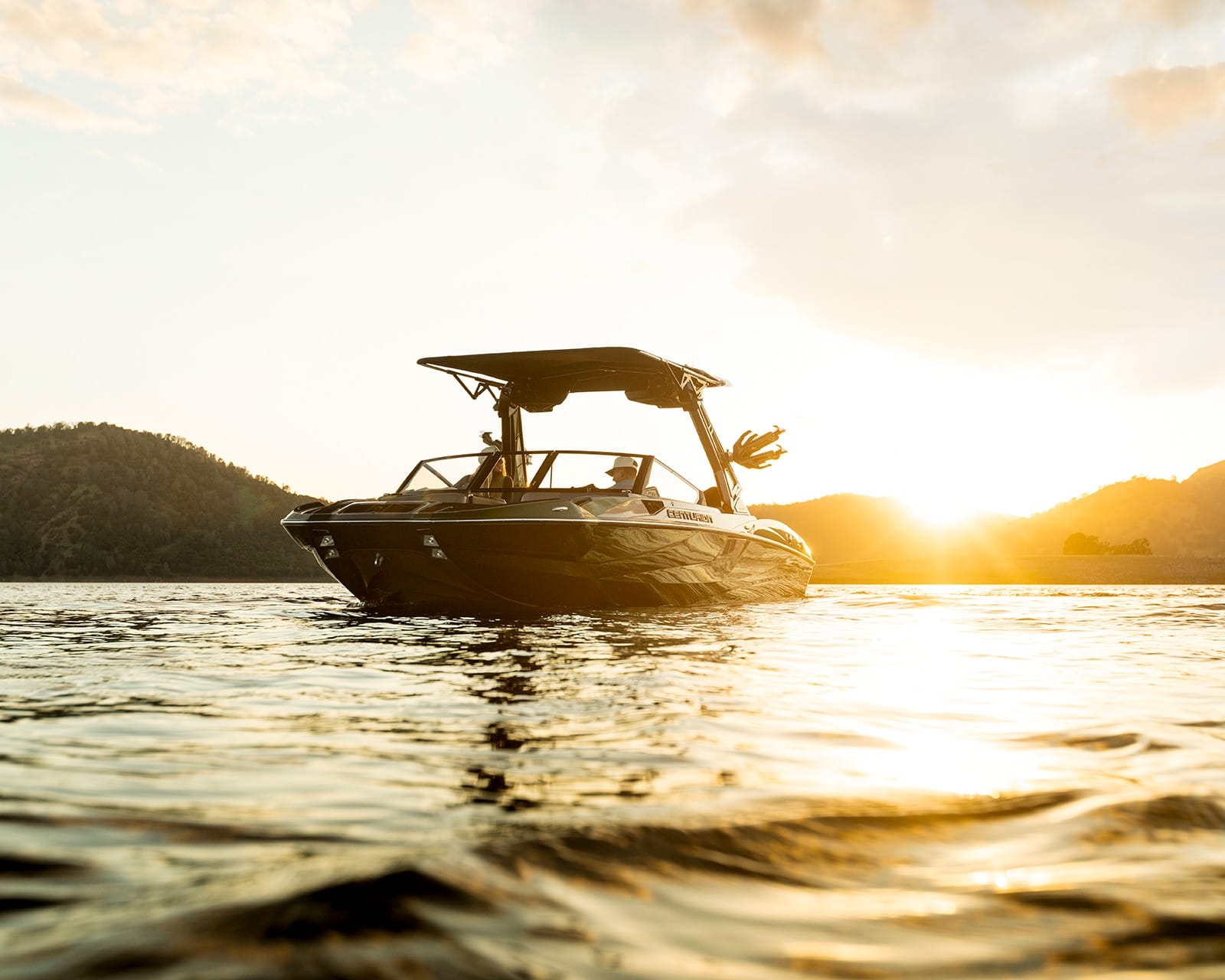 A Centurion Fi25 floats on calm water at sunset, with hills in the background and sunlight reflecting off the surface.