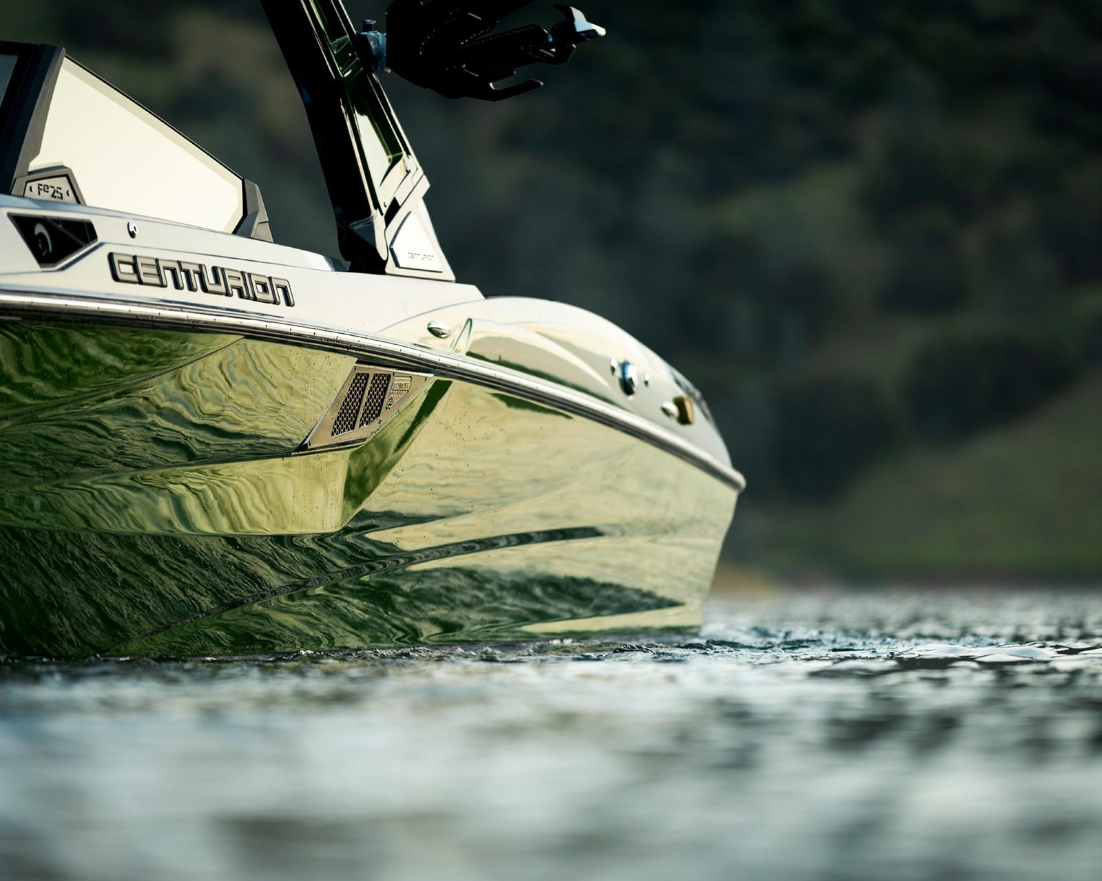 Close-up view of a Centurion Fi25 surf boat on the water, with hills visible in the blurred background.