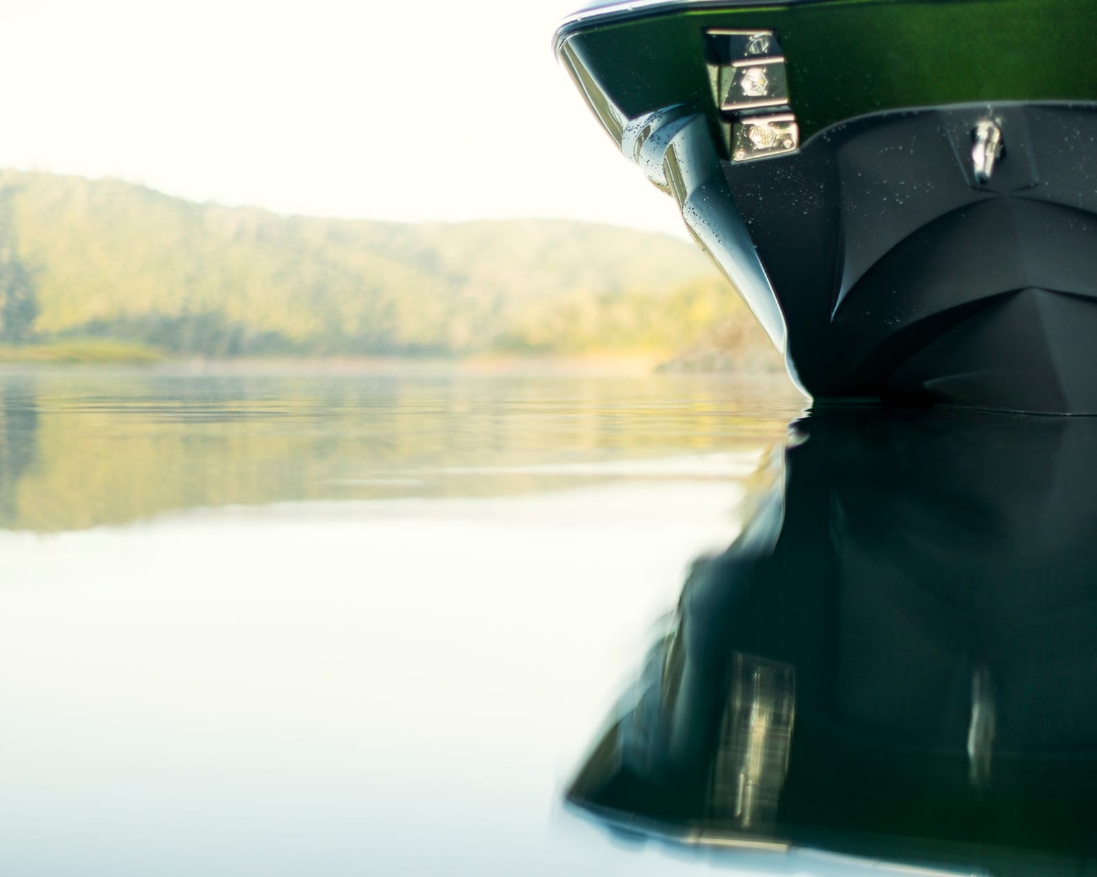 Close-up view of the bow of a Centurion Fi25 on calm water, with hills and trees visible in the blurred background.