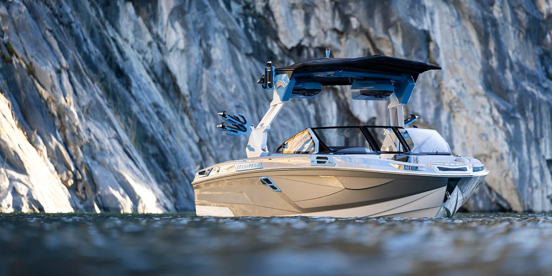 A Centurion Ri245 with a covered deck floats gracefully on calm water, framed by a rugged rocky cliff backdrop.