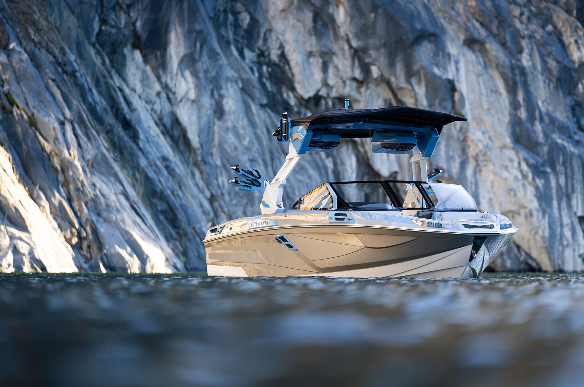 A Centurion Ri245 with a covered deck floats gracefully on calm water, framed by a rugged rocky cliff backdrop.