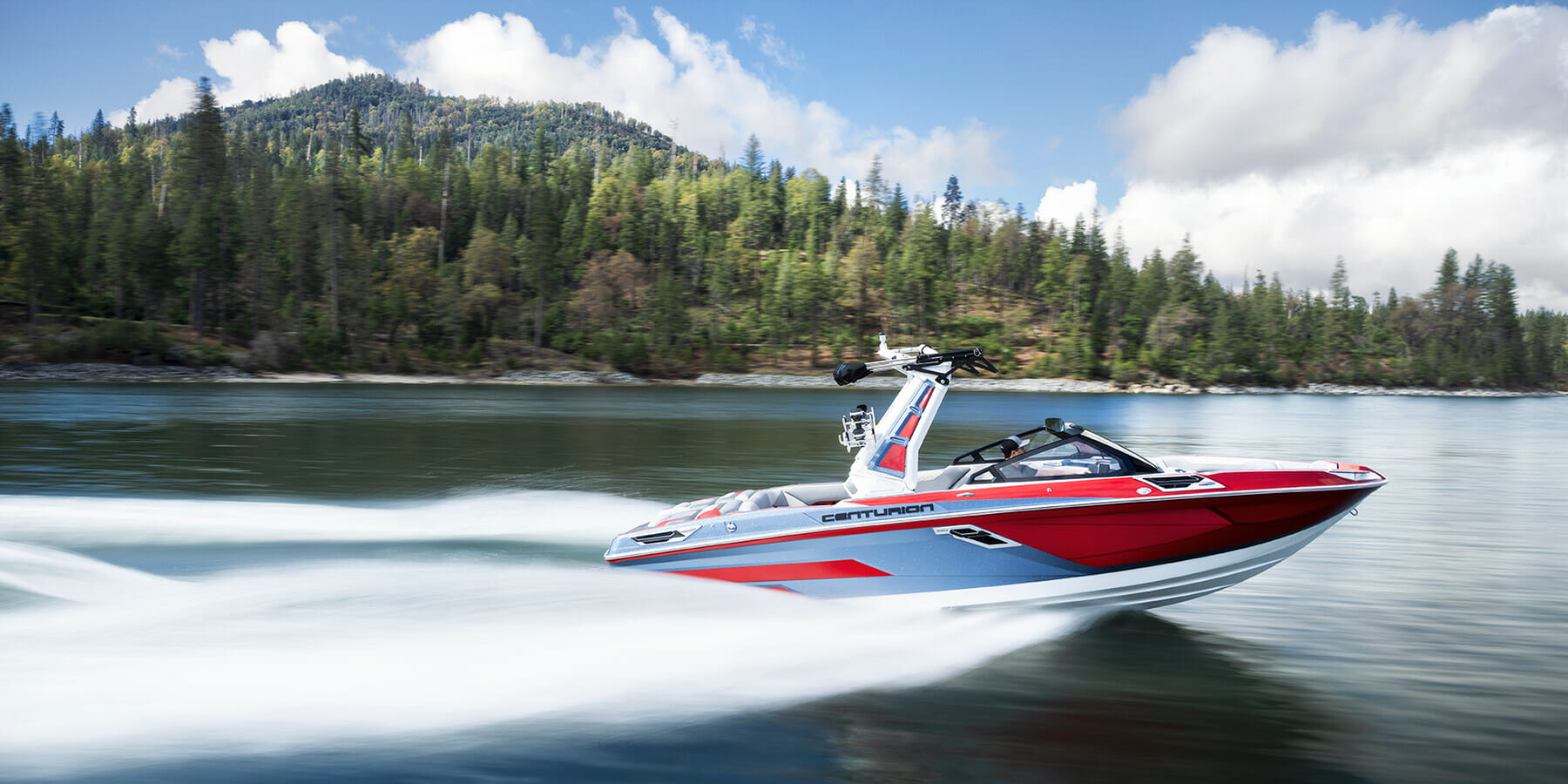 A red and white wakeboat speeding through a body of water.