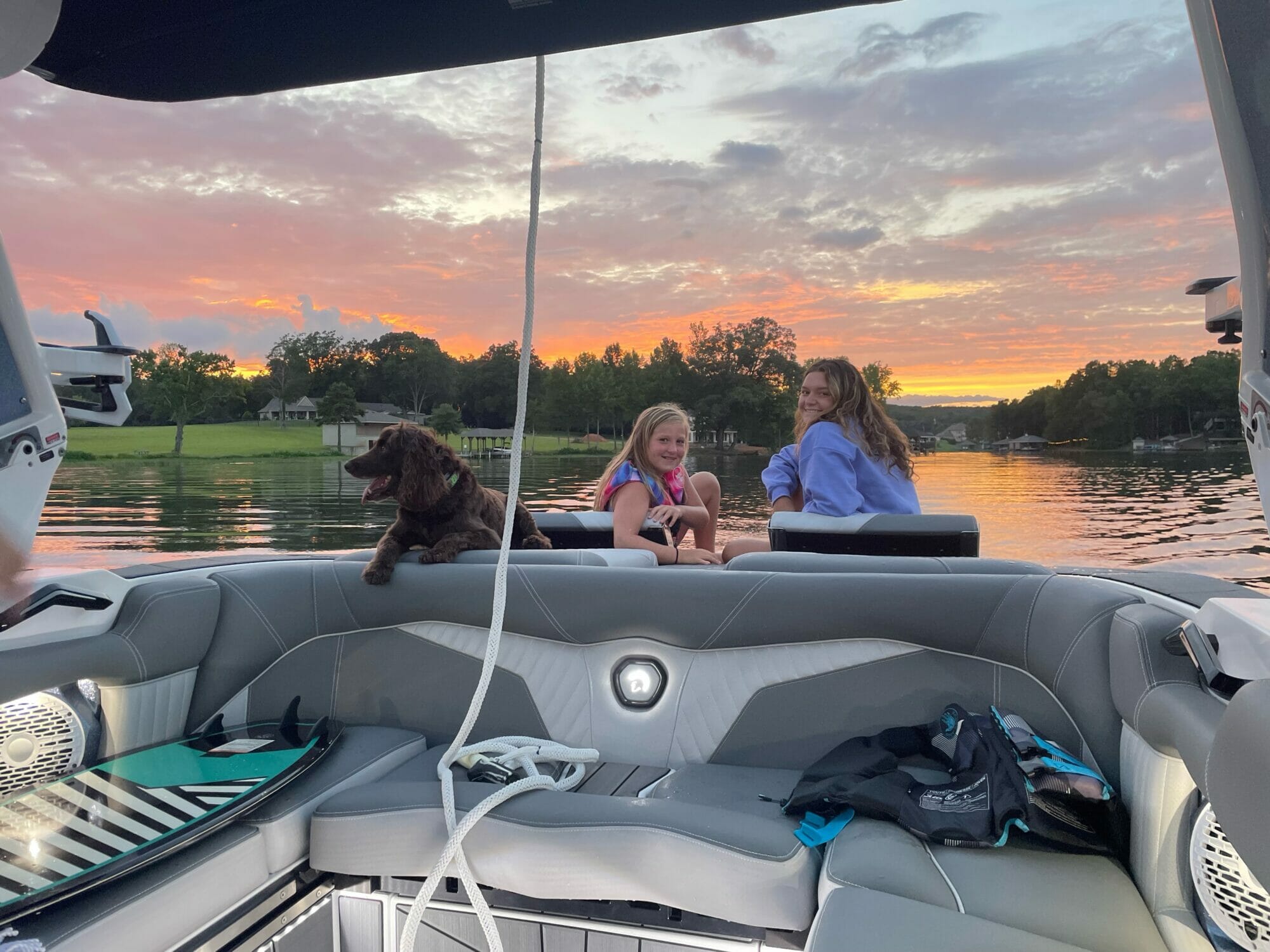 Two girls and a dog enjoying the sunset on a wakeboat.
