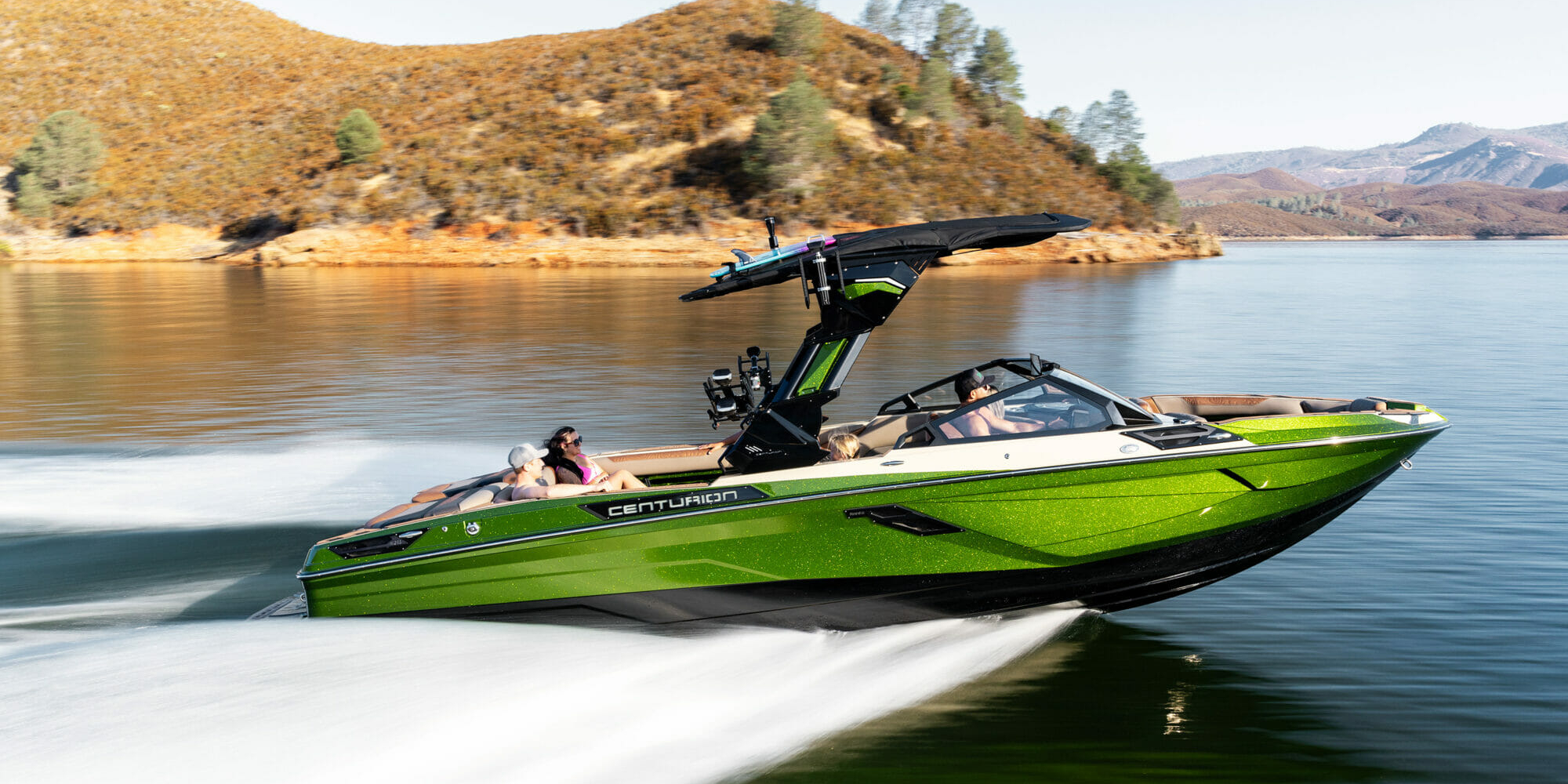 A green wakeboat is speeding through a body of water.