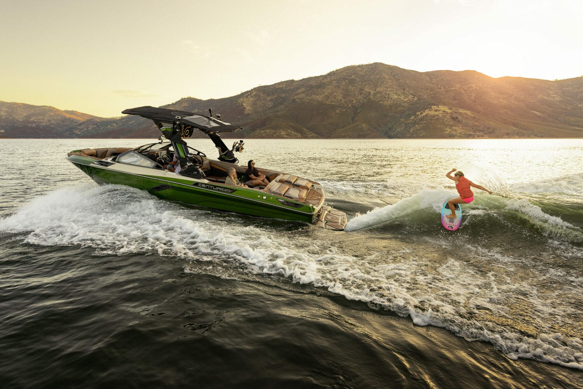 A woman is riding a wakesurf board on a green boat.