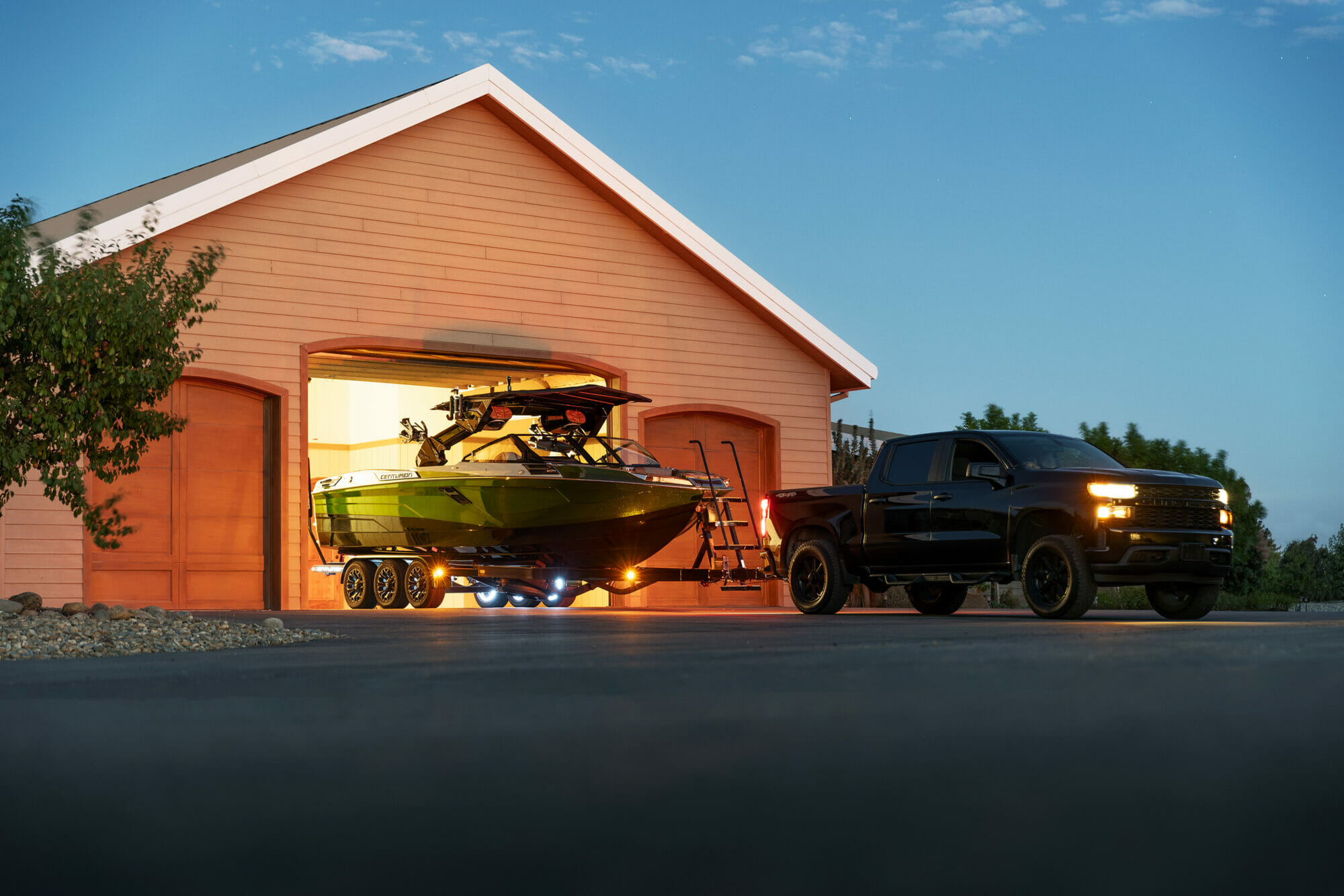A wakesurf boat parked in front of a garage.