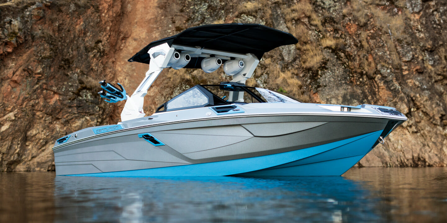 A blue wakeboat on the water near a cliff.