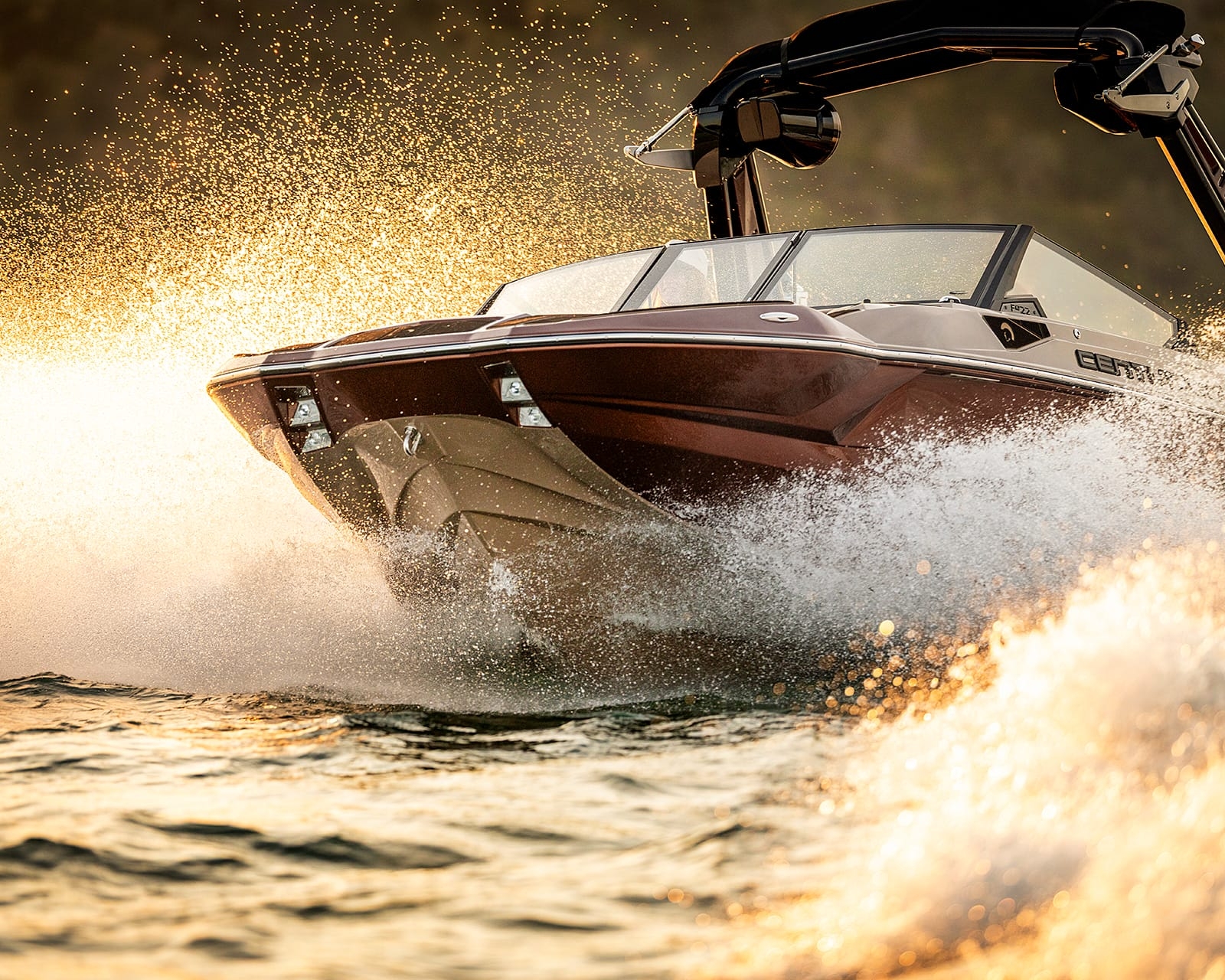 A Centurion Fe22 wake boat speeds across the water, creating splashes and spray, with sunlight reflecting off the surface and the boat’s hull.