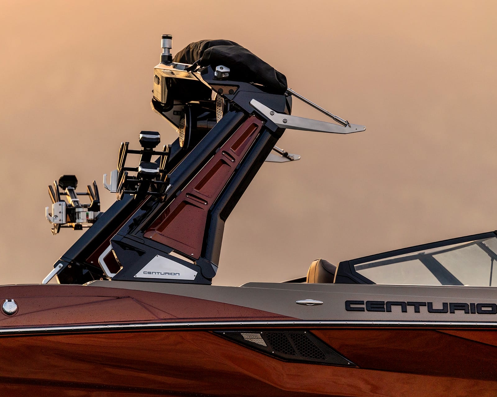 Close-up side view of a Centurion Fe22 Surf Boat with a metallic red exterior and black accents, featuring a foldable wakeboard tower and mounted equipment against a blurred beige background.