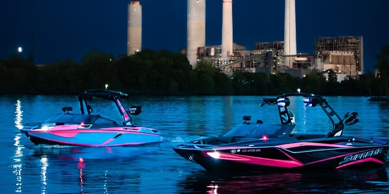 Two pink boats in the water at night near a power plant.