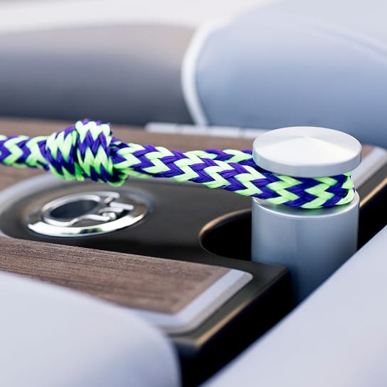 A close-up of a multicolored braided rope tied around a metal cleat on a boat deck, part of the Fe Series—highlighting personal features with rich wood and metallic details in the background.
