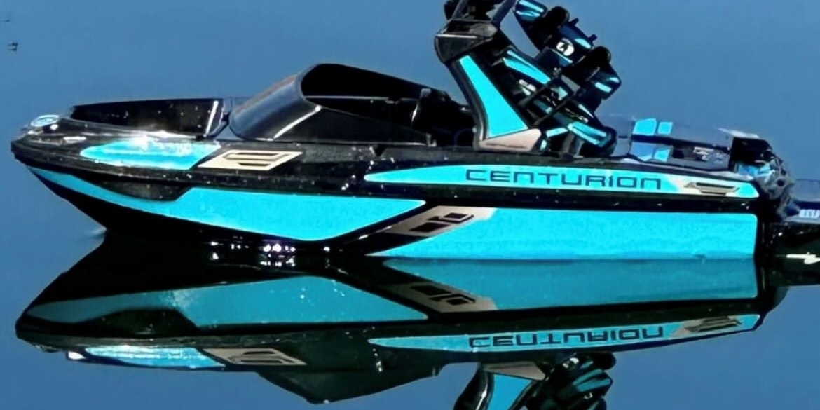 A blue Centurion wakeboard boat floats on calm water, perfectly reflecting its image.