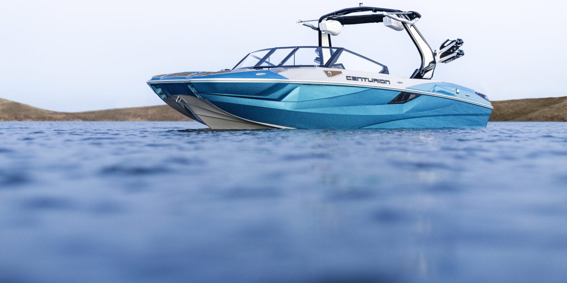 A blue and white Centurion speedboat is on the water, photographed from a low angle with distant land visible in the background.