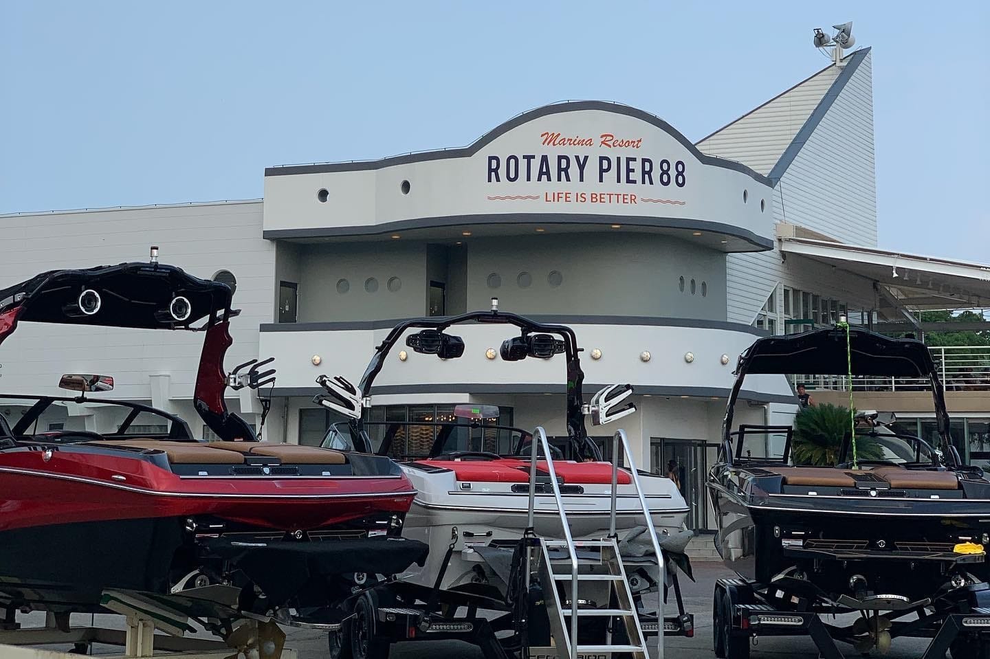 Front view of Rotary Pier 88 at Mansa Resort, showcasing several docked boats and the entrance to the pier building with signage "Life is Better.