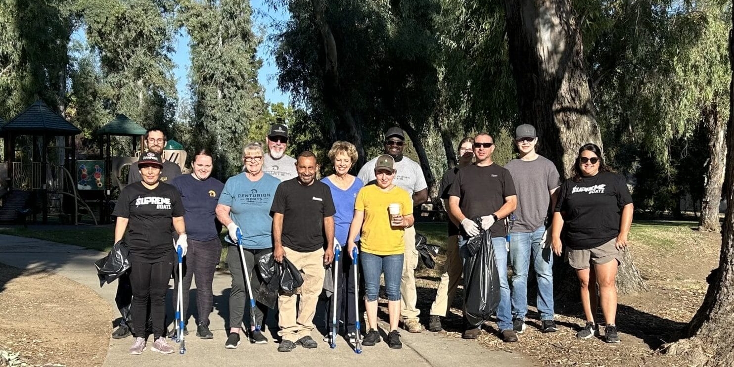 A group of people stand on a park pathway surrounded by trees, holding trash bags.