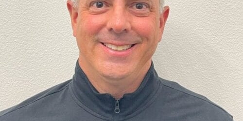 A person wearing a black zip-up jacket with the logo 