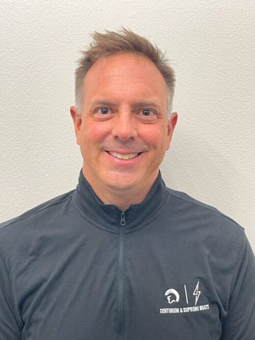 A person wearing a black zip-up jacket with the logo "Centurion & Supreme Boats" stands against a plain white background, smiling directly at the camera.