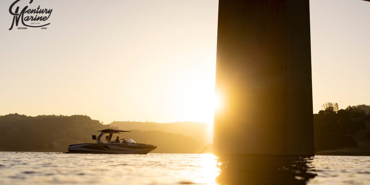 A boat cruises on a lake at sunset near a large bridge pillar, with hills in the background.