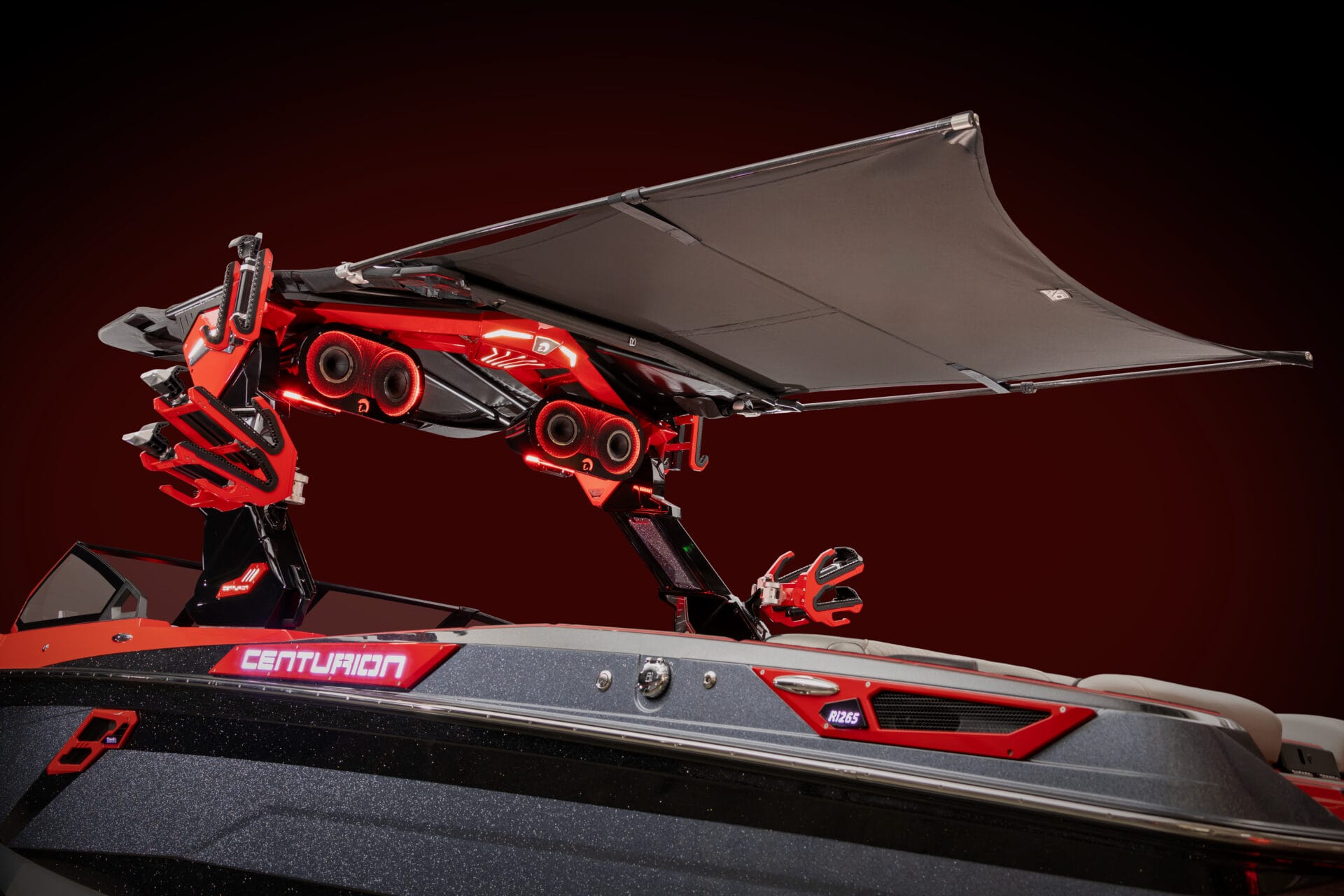 A red and black boat features advanced overhead equipment with an extended canopy. The boat's brand name, "Centurion," is visible on the side.