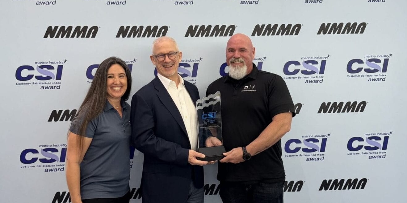 Three people stand together; the man in the center holds a trophy. They are in front of a backdrop with repeated 