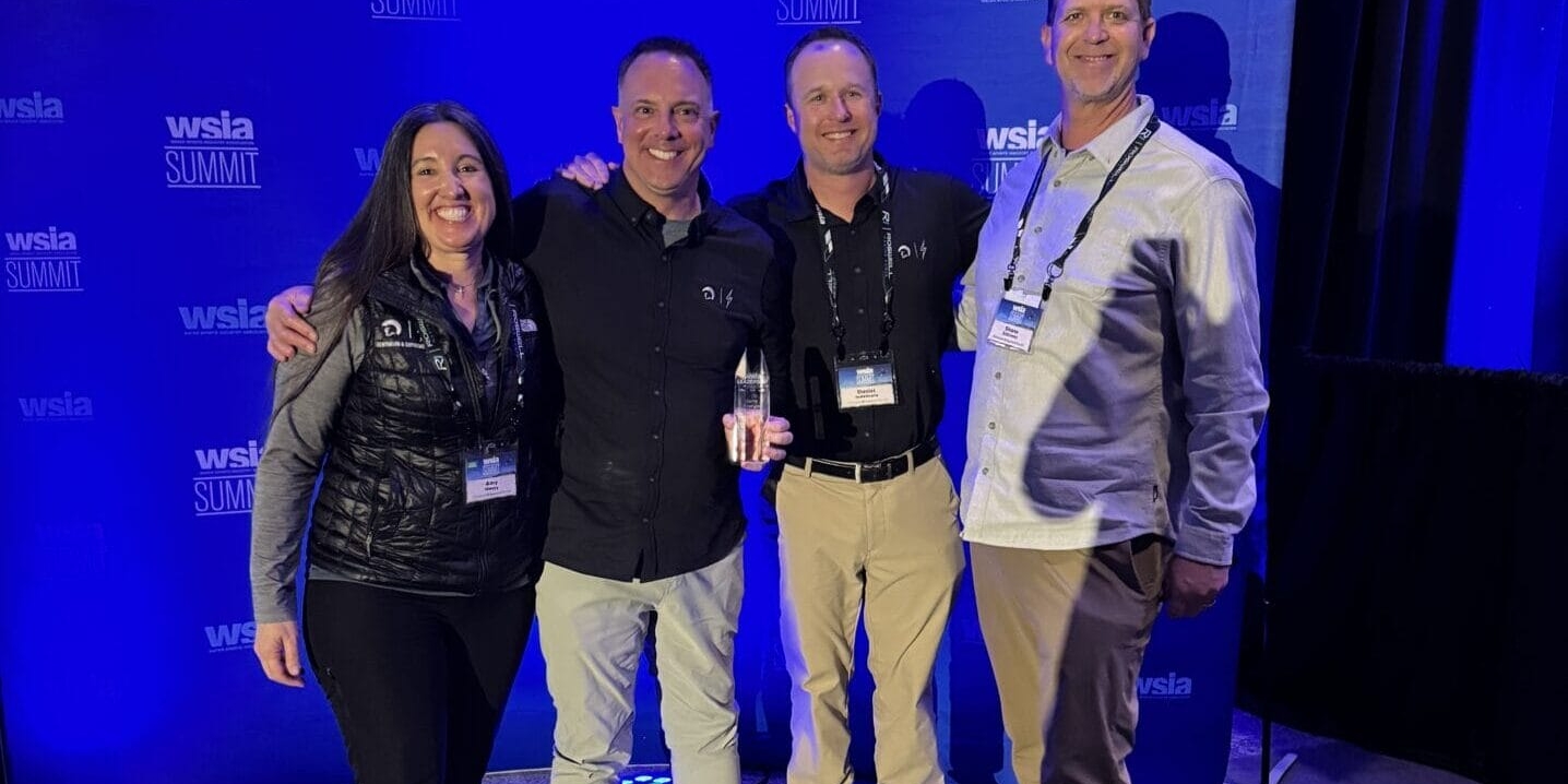 Four people smiling and posing together in front of a blue backdrop with 
