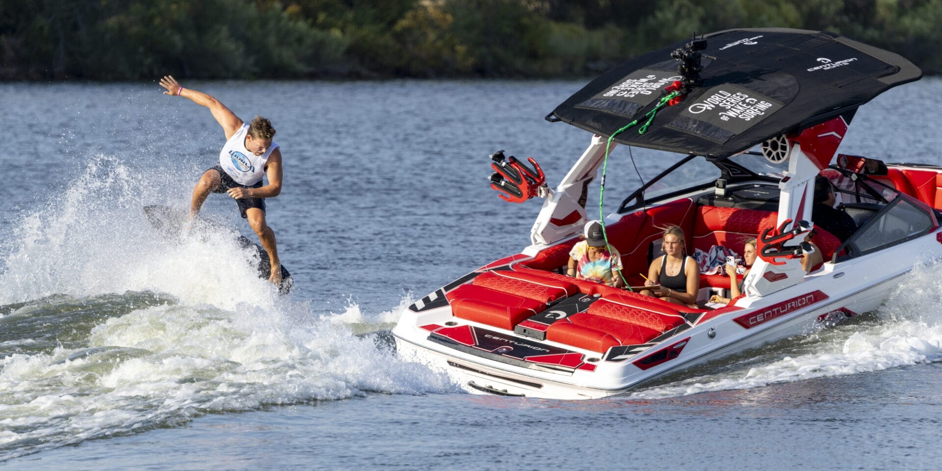 A person wakeboarding on a lake near a motorboat with passengers observing.