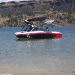 Red and white speedboat with a black canopy floating on a lake, surrounded by rocky cliffs and sparse trees.