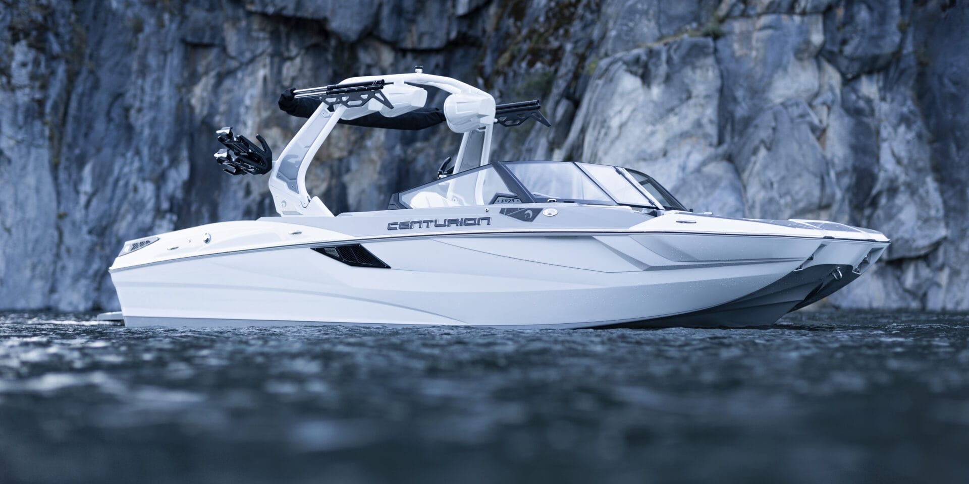 A white Centurion speedboat floats on calm water near a rocky cliff.