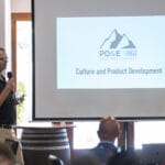 A man speaks into a microphone next to a projected slide that reads "Culture and Product Development" at the PD&E Partner Summit.