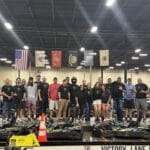 A group of people stands together indoors on a go-kart track, posing for a group photo in front of several flags and go-karts.