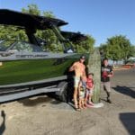 Four people stand next to a green Centurion Boats vessel and a surfboard in a parking lot on a sunny day, showing their support for the Ranger Road non-profit organization.