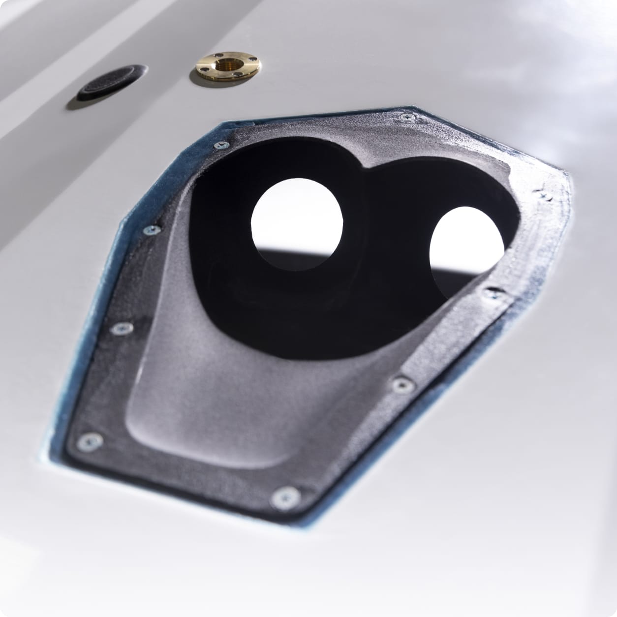 Close-up of a Centurion RAMFILL black, oval-shaped opening with two circular holes on a white surface, bordered by screws and a blue lining.