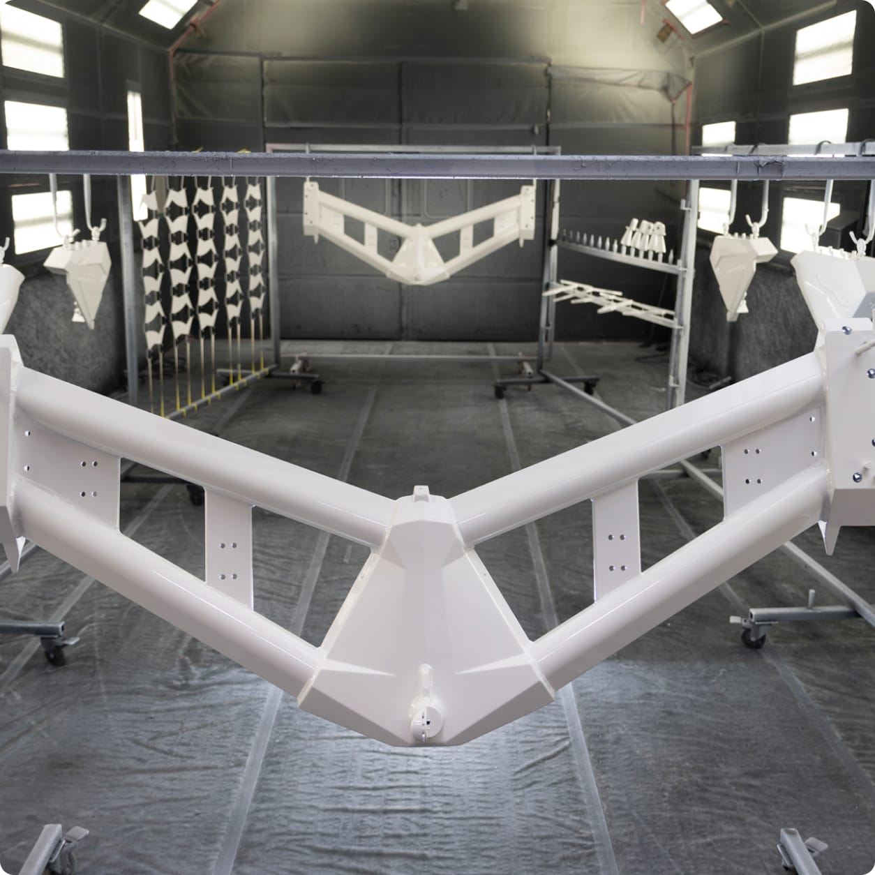 A metal frame coated in white paint hangs in a spray booth alongside other Centurion Towers components, drying in a controlled environment.