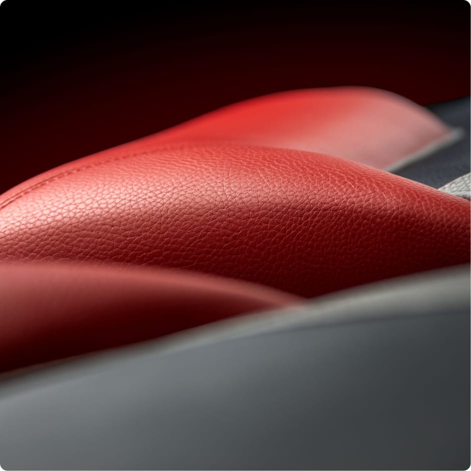 Close-up of Centurion Vinyl interior showcasing red leather car seat upholstery with visible texture and stitching, set against a blurred dark background.