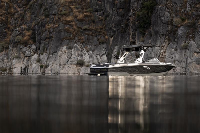 A black and white motorboat is moored on calm water near a rocky cliff with sparse vegetation.