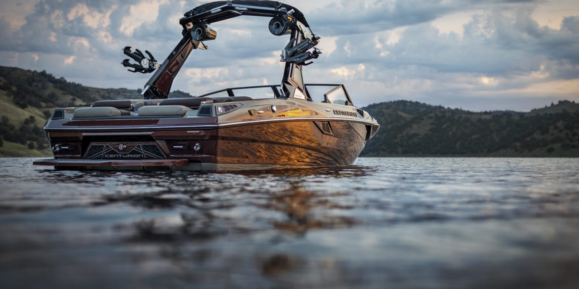 A motorboat is floating on a calm lake with hills and a cloudy sky in the background.