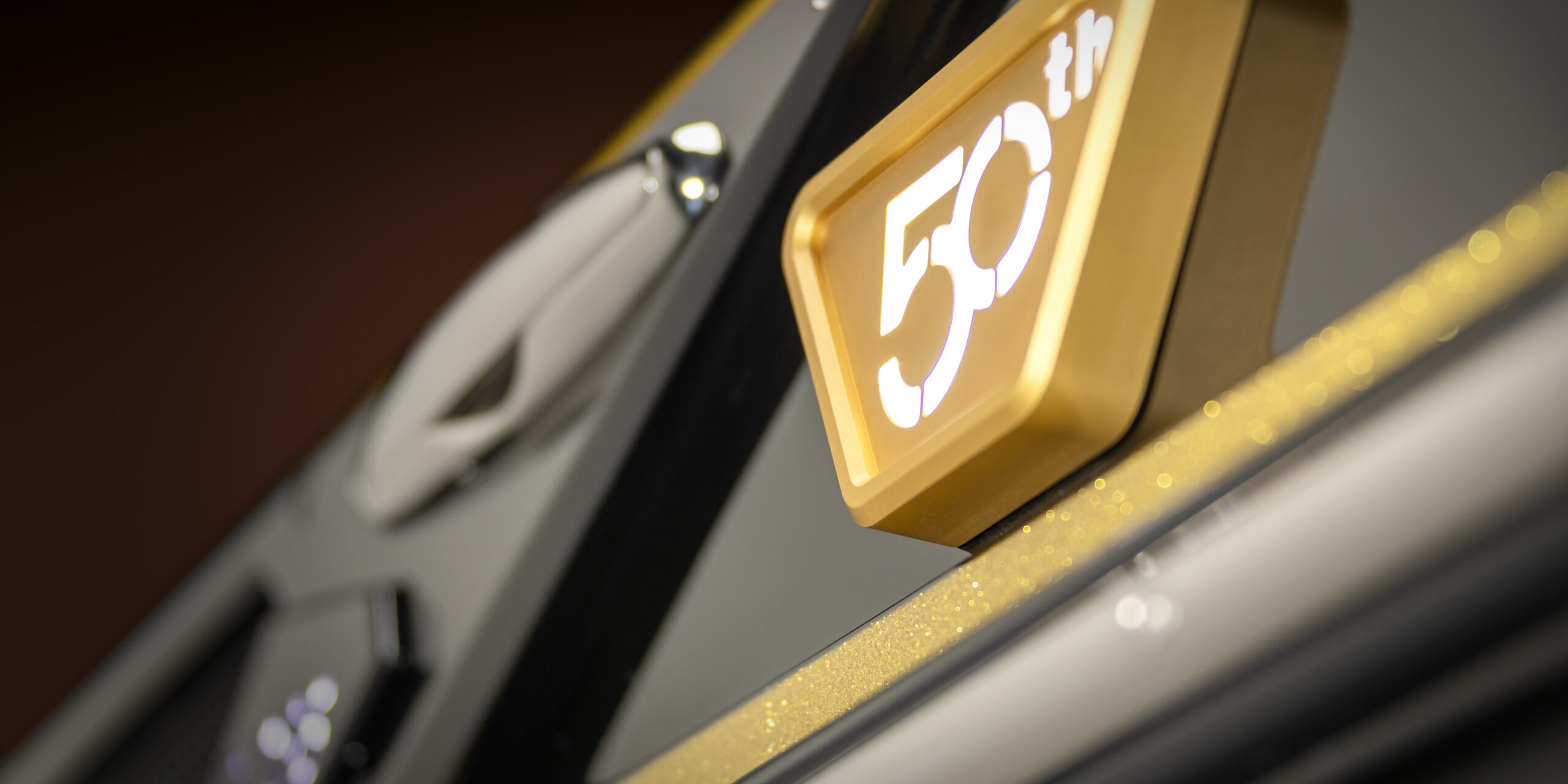 A close-up of a gold and white “50th” emblem attached to a black and metallic surface, possibly commemorating a 50th anniversary or milestone.