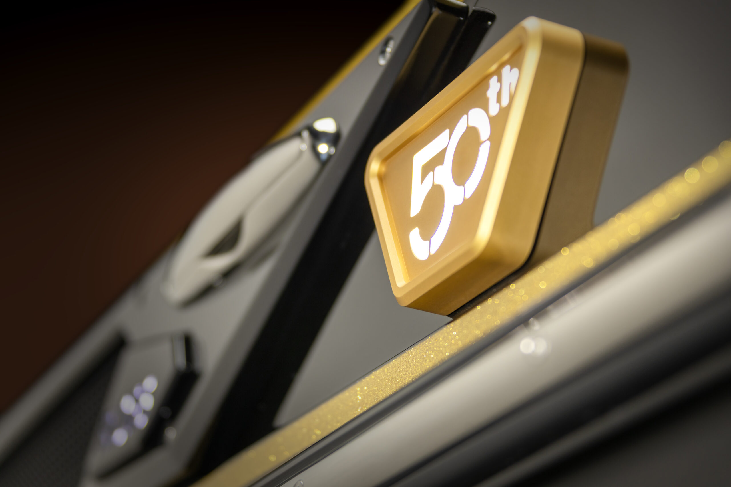 A close-up of a gold and white “50th” emblem attached to a black and metallic surface, possibly commemorating a 50th anniversary or milestone.