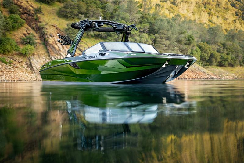 Green motorboat with black trim floating on calm water near a rocky, tree-covered shoreline.