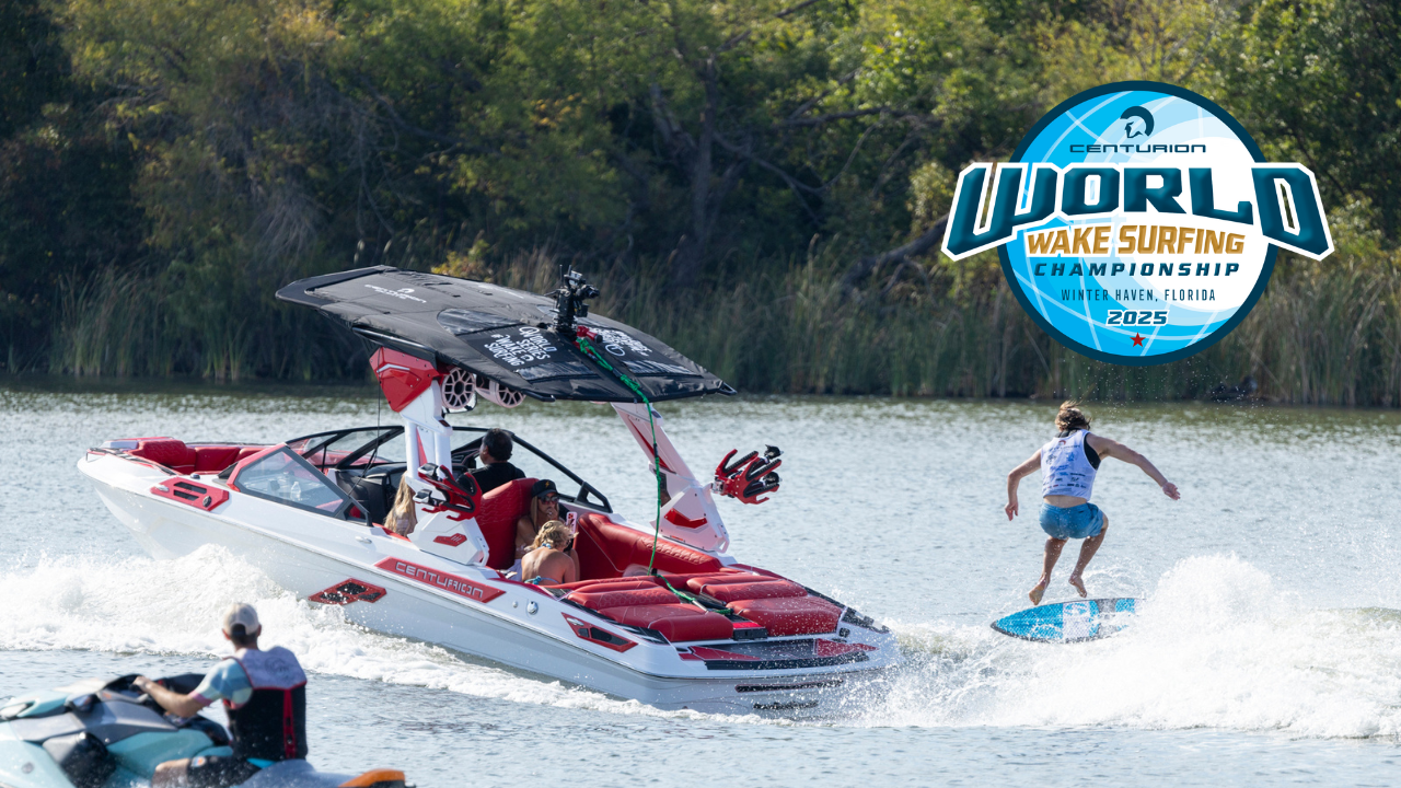 A person wake surfing behind a white and red speedboat on a lake with spectators nearby; World Wake Surfing Championship 2025 logo is displayed.