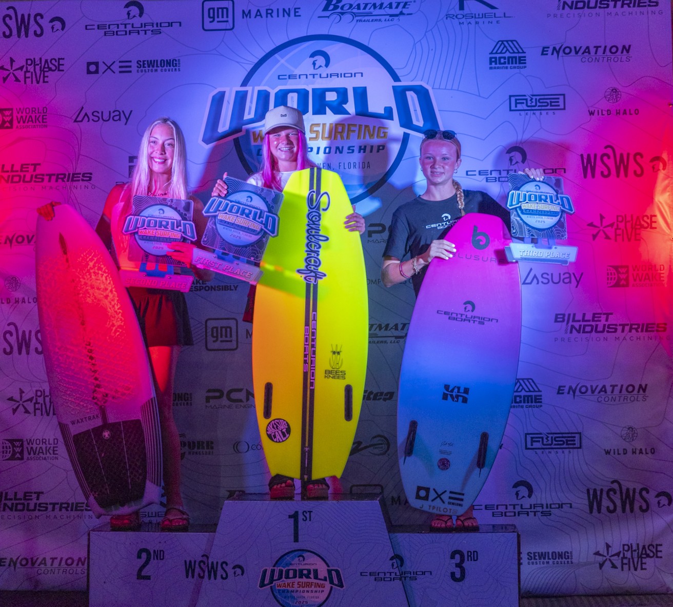 Three surfers stand on a podium holding surfboards and plaques for 1st, 2nd, and 3rd place at the Centurion World Surfing Championship, with a branded backdrop behind them.