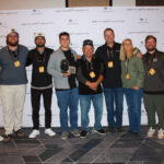 Eight people stand in a row, with one person in the center holding an award. They are posing in front of a Centurion Boats branded backdrop.