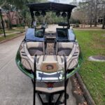 A parked Centurion boat on a residential street, viewed from the rear, showing cushioned seating, speakers, and neighborhood houses in the background.