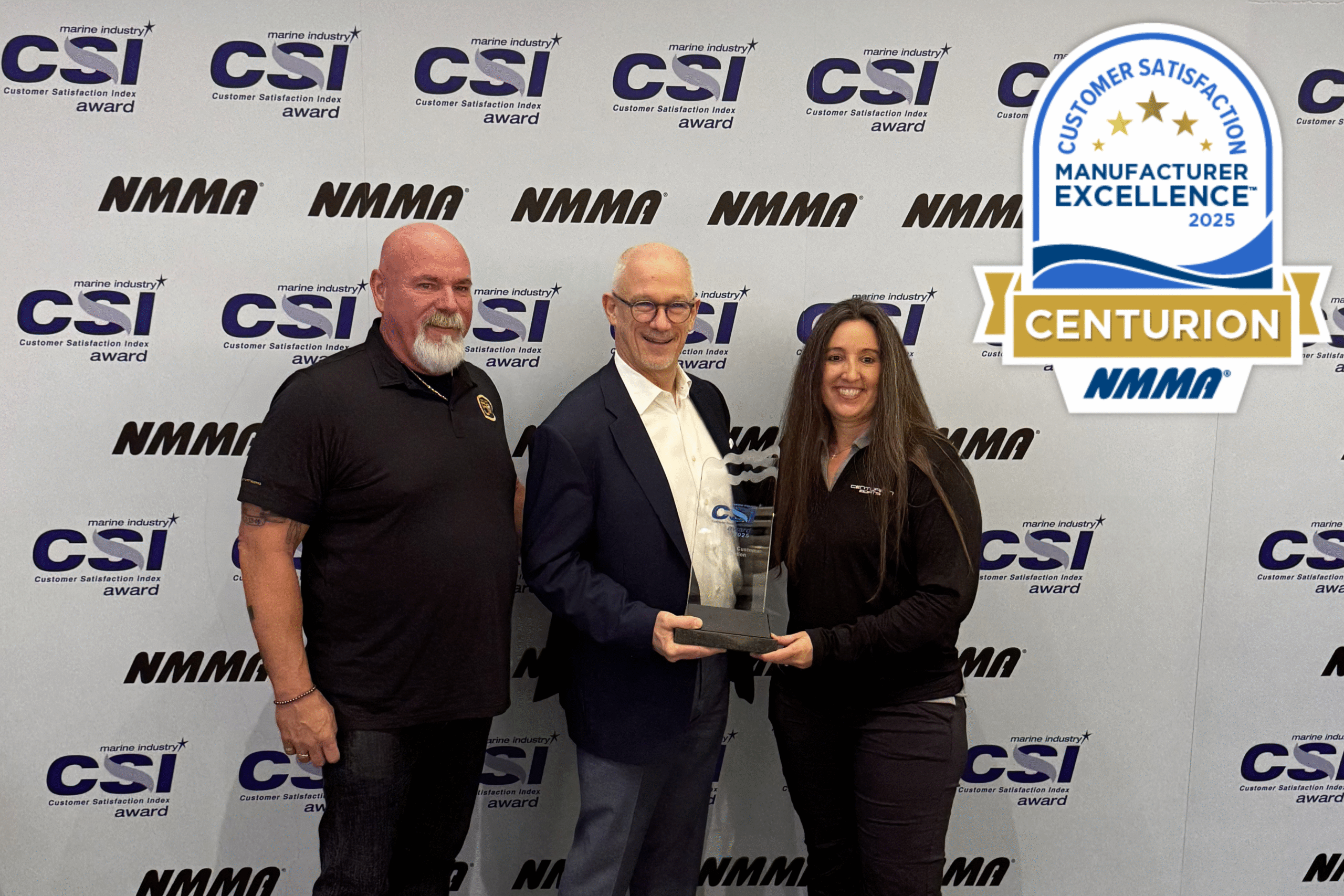 Three people pose together holding a glass award in front of a backdrop with CSI and NMMA logos; a 