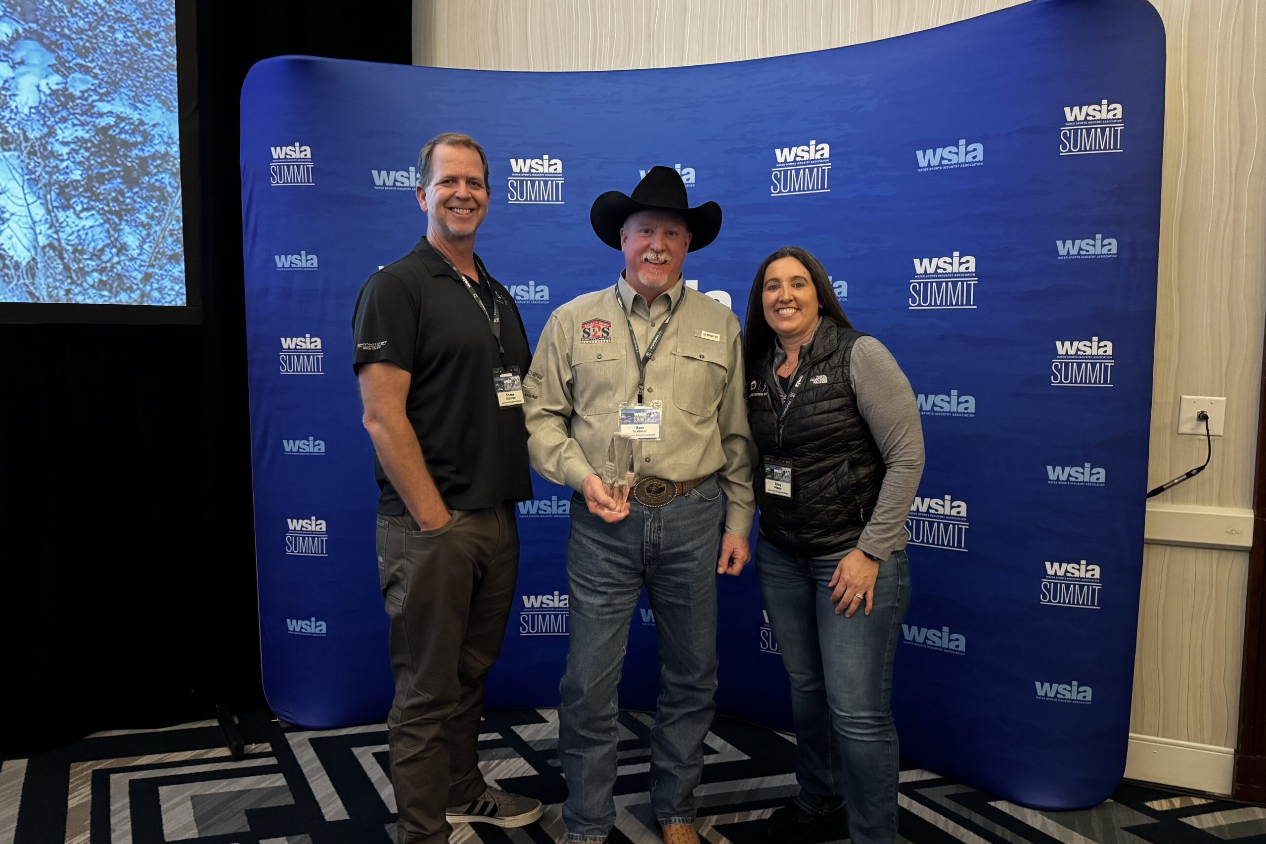 Three people pose together in front of a blue 